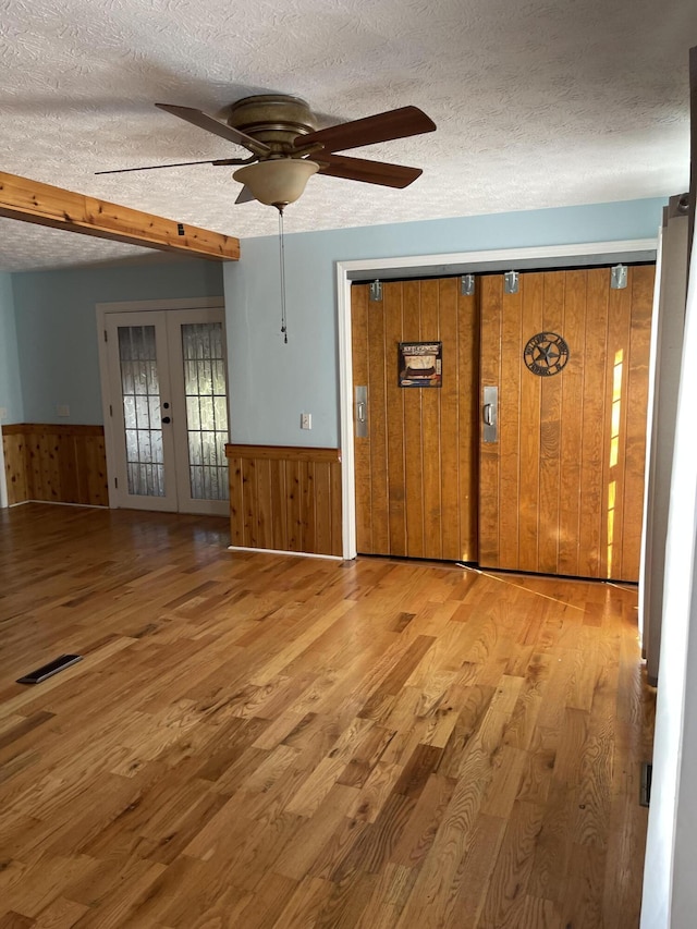 interior space featuring french doors, wooden walls, hardwood / wood-style flooring, ceiling fan, and a textured ceiling