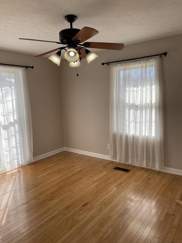 empty room featuring baseboards, a textured ceiling, visible vents, hardwood / wood-style floors, and ceiling fan
