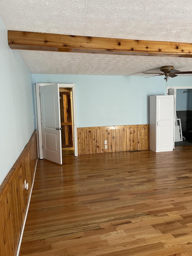 empty room featuring ceiling fan, dark hardwood / wood-style flooring, beamed ceiling, a textured ceiling, and wooden walls