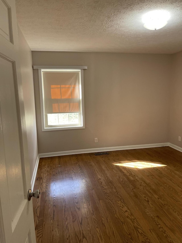 empty room with baseboards, wood finished floors, and a textured ceiling
