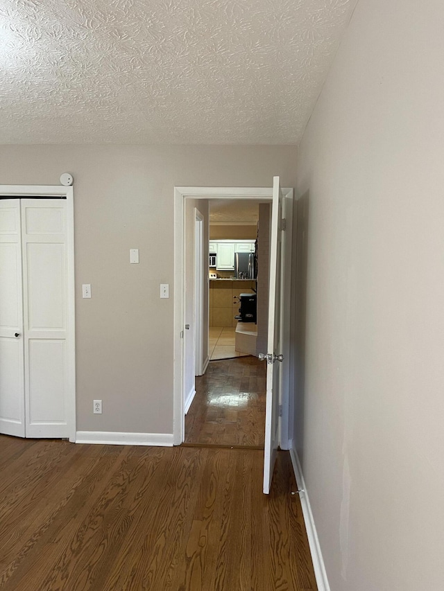corridor featuring dark wood-type flooring, a textured ceiling, and baseboards