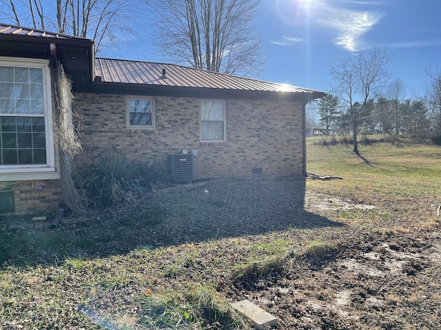 view of side of property featuring central AC unit, brick siding, metal roof, and crawl space