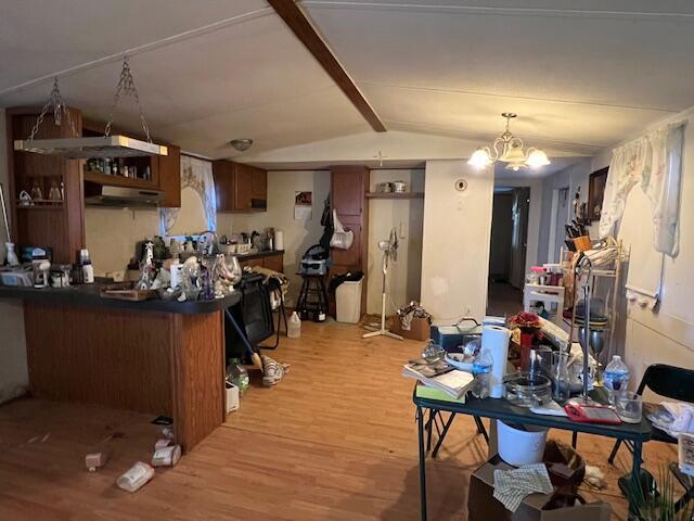 kitchen featuring a notable chandelier, light hardwood / wood-style floors, kitchen peninsula, and vaulted ceiling