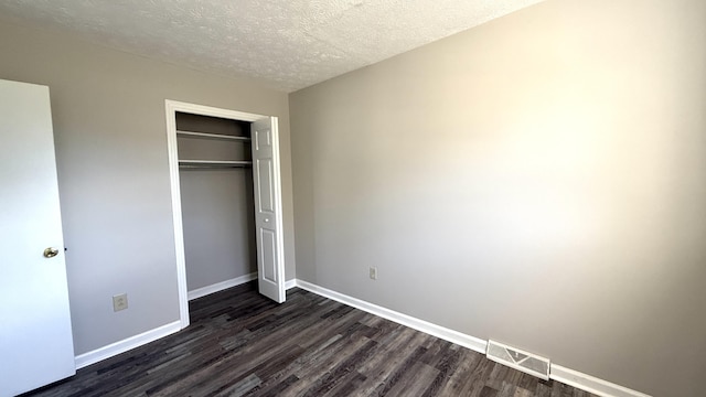 unfurnished bedroom featuring a textured ceiling, dark hardwood / wood-style flooring, and a closet