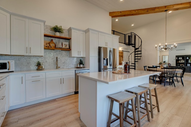 kitchen featuring beam ceiling, white cabinetry, light wood-type flooring, and appliances with stainless steel finishes