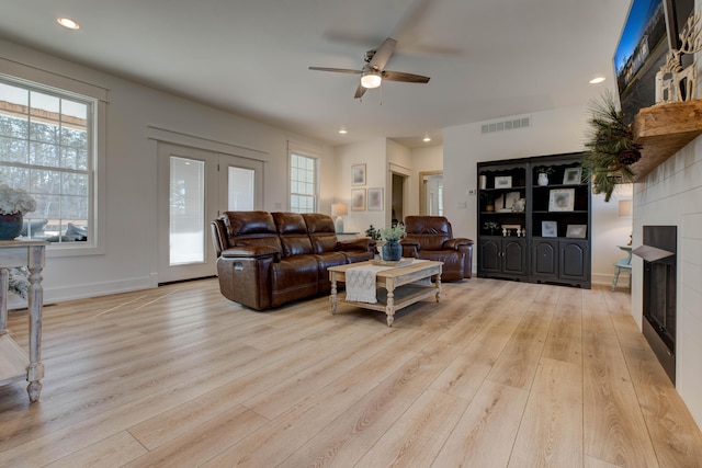 living room with a tile fireplace, light hardwood / wood-style floors, and ceiling fan