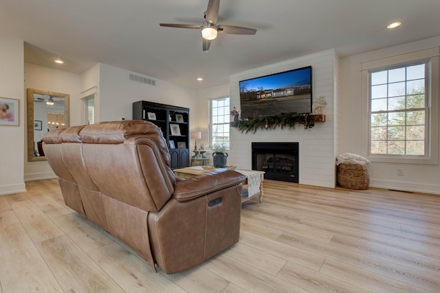 living room featuring a large fireplace, light hardwood / wood-style floors, and ceiling fan