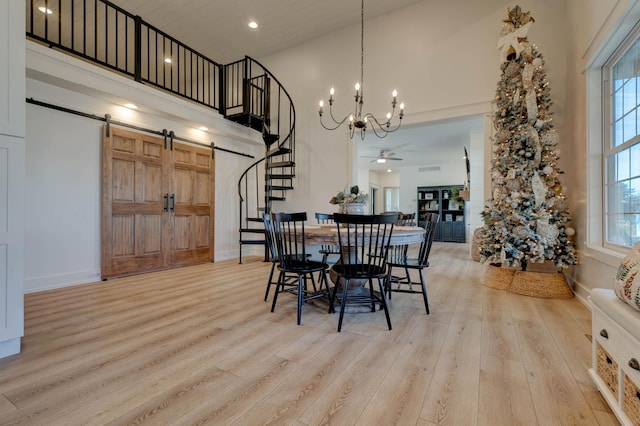 dining room with a barn door, light hardwood / wood-style flooring, ceiling fan with notable chandelier, and a high ceiling