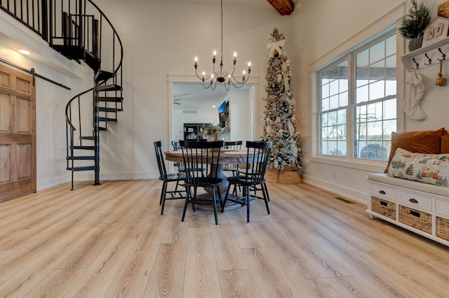 dining room featuring a towering ceiling, a barn door, light hardwood / wood-style floors, and an inviting chandelier