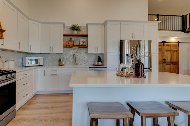 kitchen featuring a barn door, white cabinets, light hardwood / wood-style floors, and appliances with stainless steel finishes