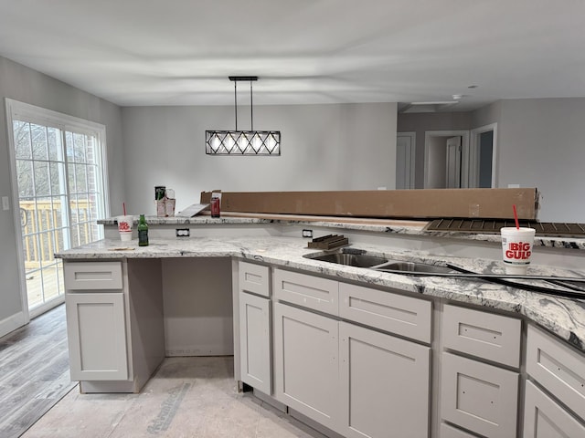 kitchen with light stone counters, sink, white cabinetry, and hanging light fixtures