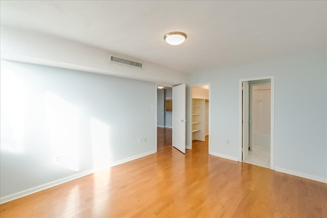 unfurnished bedroom featuring ensuite bath, a spacious closet, a closet, and light hardwood / wood-style floors