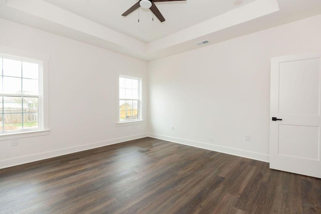 spare room with a tray ceiling, visible vents, baseboards, ceiling fan, and dark wood-type flooring
