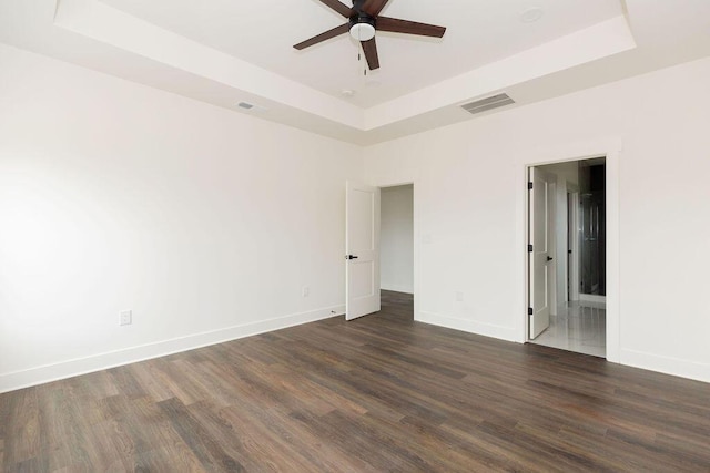 spare room featuring ceiling fan, dark wood-type flooring, a tray ceiling, and visible vents