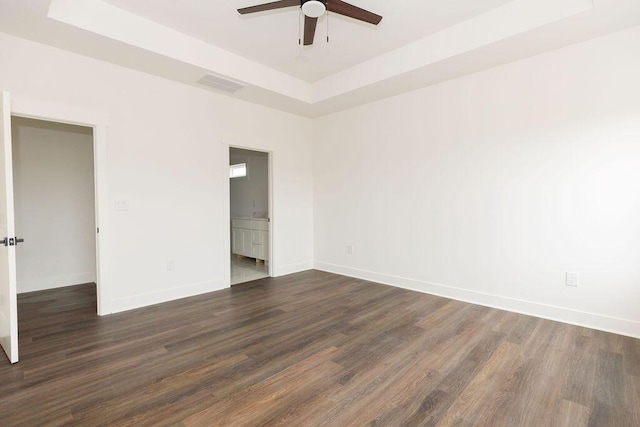 unfurnished bedroom with dark wood-style floors, baseboards, visible vents, connected bathroom, and a raised ceiling