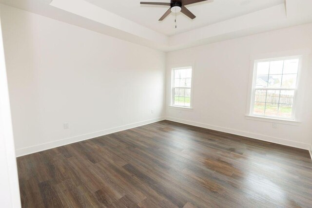 spare room featuring a ceiling fan, baseboards, a raised ceiling, and dark wood-style flooring