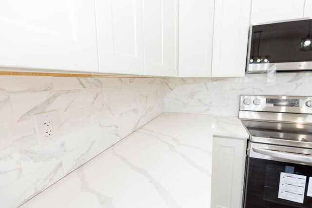 kitchen featuring white cabinets, stainless steel appliances, decorative backsplash, and light stone countertops