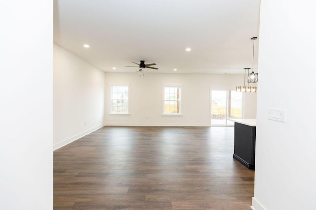 empty room with ceiling fan with notable chandelier, baseboards, recessed lighting, and dark wood-style flooring