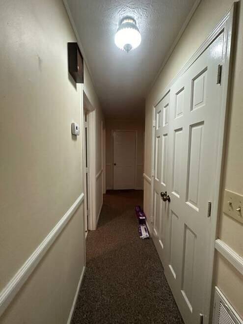 corridor with a textured ceiling and dark colored carpet