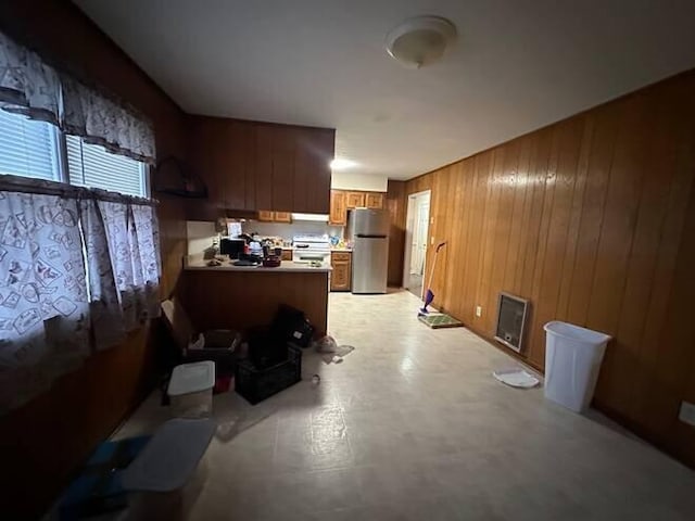 kitchen with kitchen peninsula, white range oven, extractor fan, wooden walls, and stainless steel refrigerator