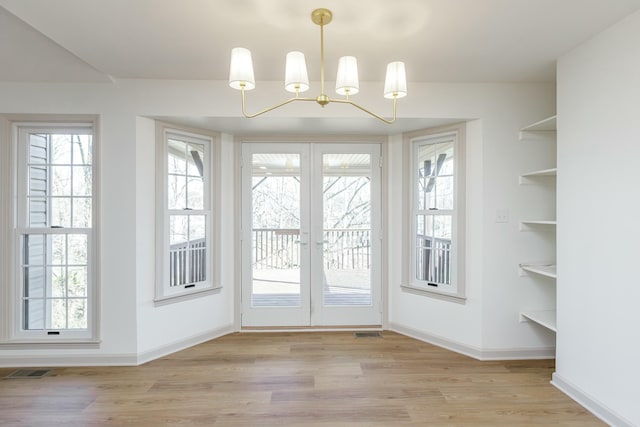 doorway with light hardwood / wood-style floors, built in features, french doors, and an inviting chandelier