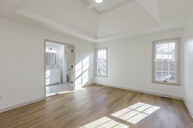 empty room with light wood-type flooring, a tray ceiling, and ceiling fan