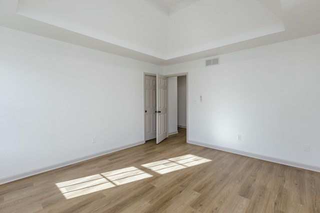 unfurnished room featuring a raised ceiling, a high ceiling, and light wood-type flooring