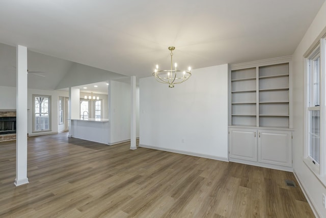 unfurnished dining area with hardwood / wood-style flooring, ceiling fan with notable chandelier, a fireplace, and vaulted ceiling