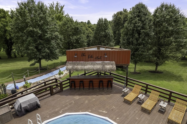 exterior space featuring a lawn, a wooden deck, a grill, and an outdoor bar