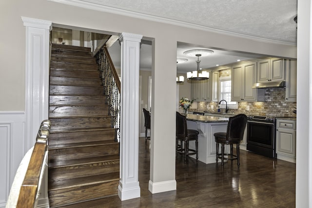 stairway featuring decorative columns, hardwood / wood-style floors, a textured ceiling, and ornamental molding