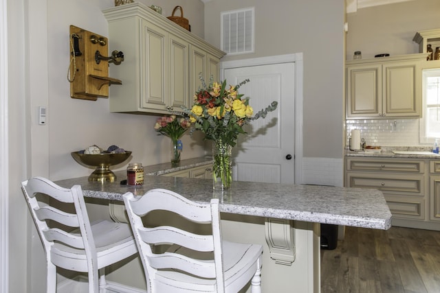 interior space featuring kitchen peninsula, dark hardwood / wood-style flooring, tasteful backsplash, and a breakfast bar area