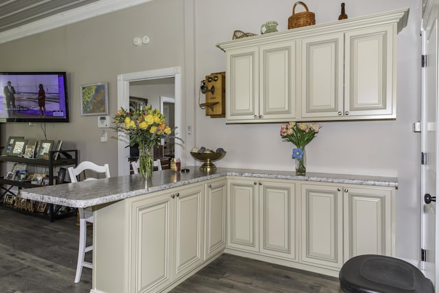 kitchen with kitchen peninsula, a breakfast bar, dark wood-type flooring, crown molding, and cream cabinetry