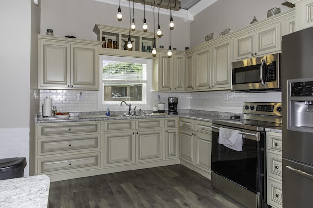 kitchen with cream cabinets, crown molding, hanging light fixtures, appliances with stainless steel finishes, and light stone counters