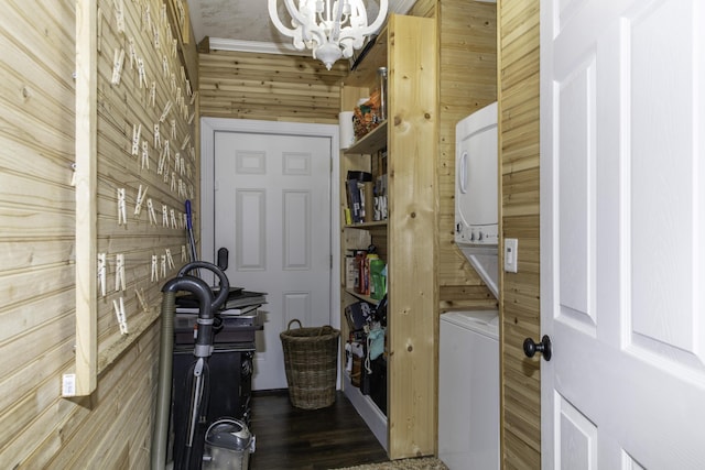 laundry area featuring an inviting chandelier, stacked washer and clothes dryer, and wood walls