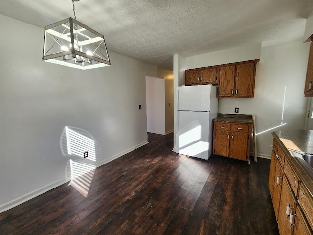 kitchen with dark wood-type flooring, hanging light fixtures, a textured ceiling, a notable chandelier, and white fridge