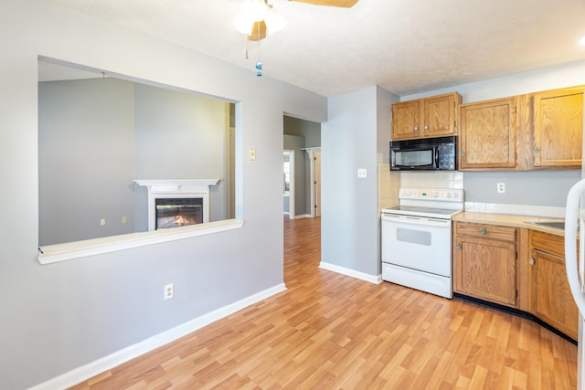 kitchen with white range with electric stovetop, light wood finished floors, light countertops, a glass covered fireplace, and black microwave