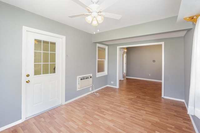 empty room with light wood-type flooring, ceiling fan, baseboards, and a wall mounted AC