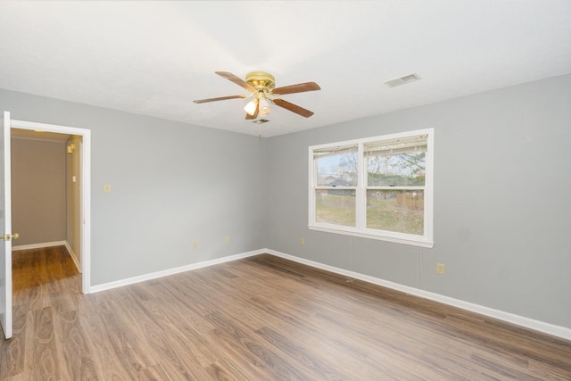 empty room featuring a ceiling fan, wood finished floors, visible vents, and baseboards