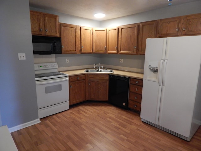 kitchen with black appliances, brown cabinetry, light wood-type flooring, and a sink