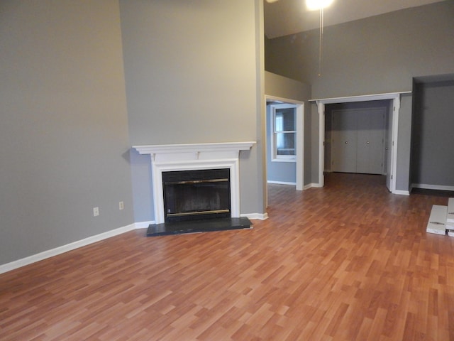 unfurnished living room featuring baseboards, a fireplace with raised hearth, and wood finished floors