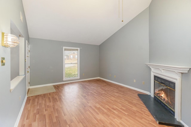 unfurnished living room featuring light wood-style floors, a glass covered fireplace, vaulted ceiling, and baseboards