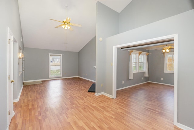 unfurnished living room with high vaulted ceiling, ceiling fan, baseboards, and light wood-style flooring