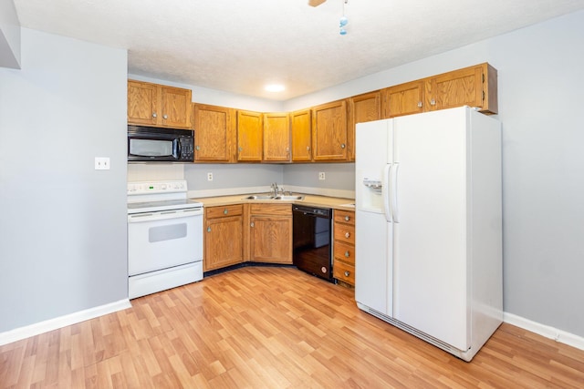 kitchen with light wood-type flooring, black appliances, brown cabinetry, and a sink