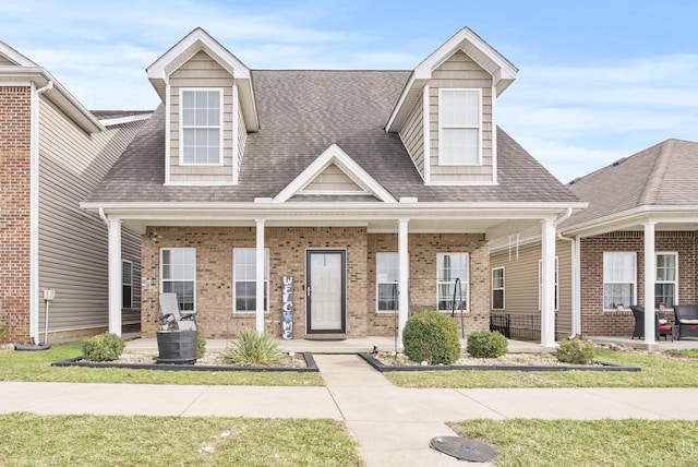 view of front facade with brick siding, a porch, and a shingled roof