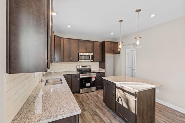 kitchen featuring sink, backsplash, appliances with stainless steel finishes, a center island, and light stone counters