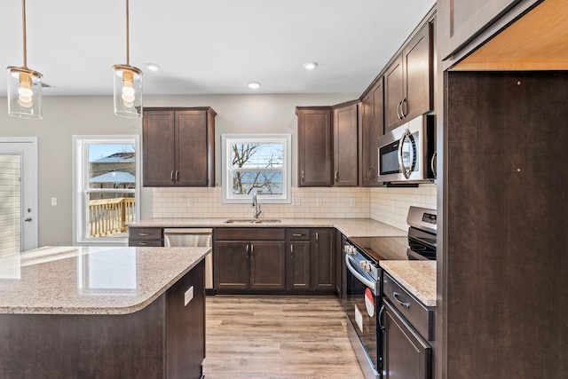 kitchen with sink, stainless steel appliances, pendant lighting, light stone countertops, and decorative backsplash