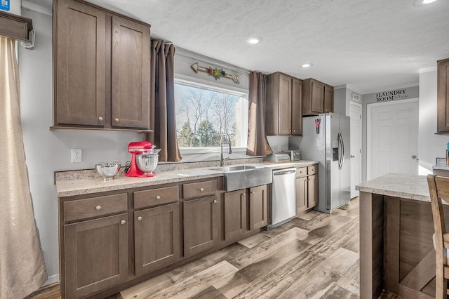 kitchen featuring dark brown cabinets, sink, stainless steel appliances, and light hardwood / wood-style flooring