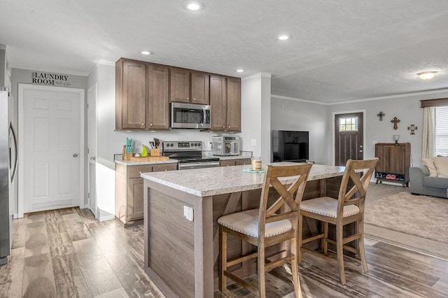 kitchen featuring crown molding, a breakfast bar area, light hardwood / wood-style flooring, a kitchen island, and stainless steel appliances