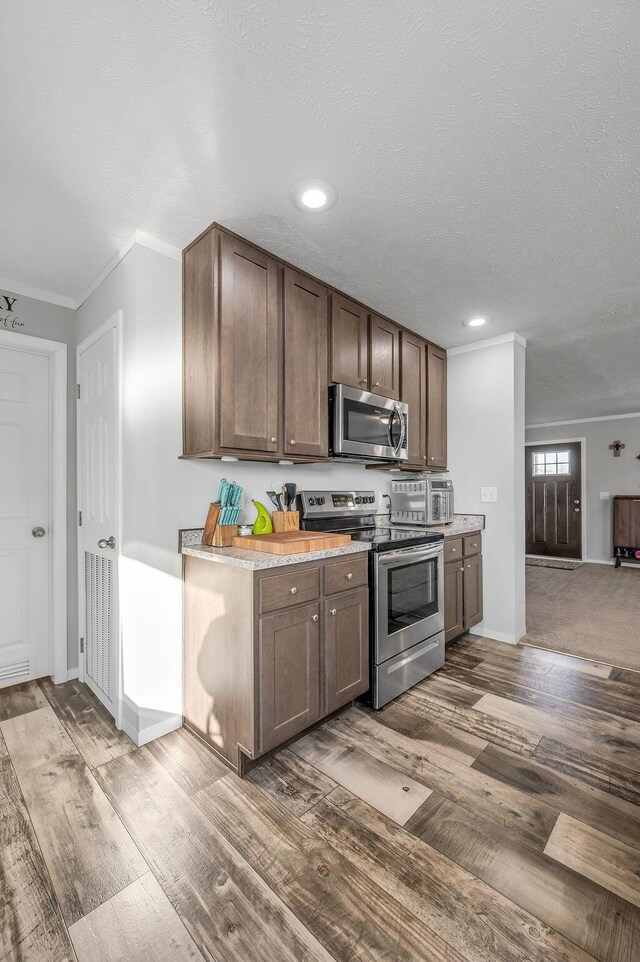 kitchen featuring hardwood / wood-style flooring, ornamental molding, a textured ceiling, dark brown cabinetry, and stainless steel appliances