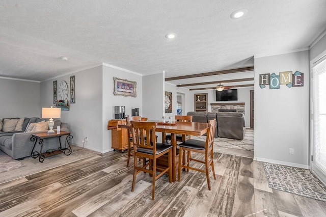 dining room featuring ceiling fan, a fireplace, wood-type flooring, and a textured ceiling